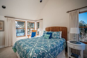 A bedroom with a large bed, a bedside table, a window with curtains, and a view of the outdoors.