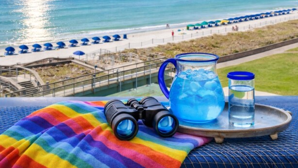 Blick auf einen Strand mit blauem Himmel, Wasser und Sonnenschirmen.
