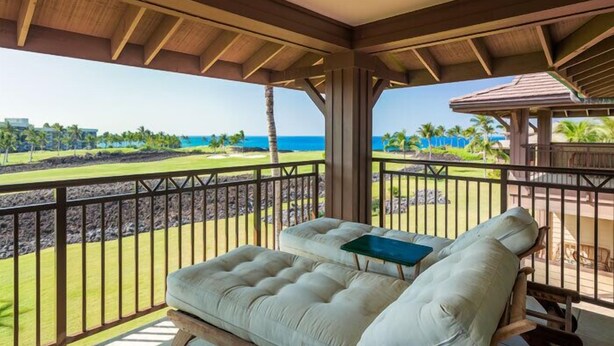 A balcony with a cushioned seating area, a view of a golf course, and a clear blue sky. - 3 Bedroom Ocean View Townhome (Waikoloa)
