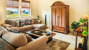 A living room with a sofa, a coffee table, a cabinet, and a view of the ocean through two windows. - 3 Bedroom Ocean View Townhome (Waikoloa)