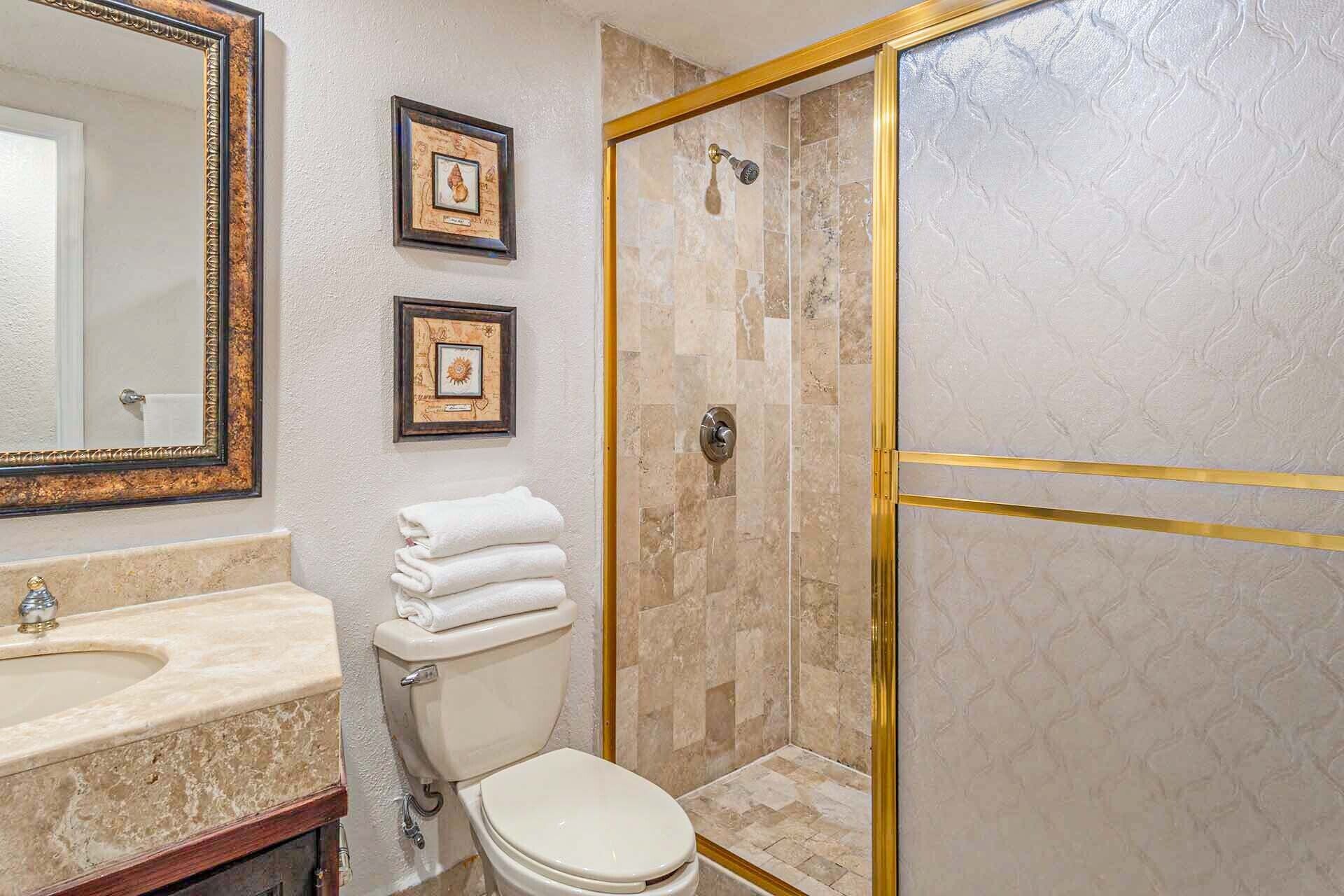 Ein Badezimmer mit einem großen Spiegel, zwei gerahmten Bildern, einer Toilette und einer Dusche mit goldener Rahmung.