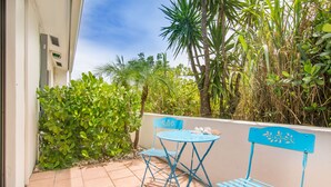 Un patio al aire libre con una mesa y sillas de metal azul, rodeado de abundante vegetación y un muro blanco.