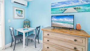 Una habitación con escritorio, dos sillas, televisor y un objeto decorativo en una cómoda.