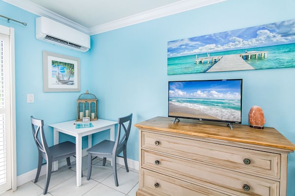 A room with a desk, two chairs, a television, and a decorative item on a dresser.