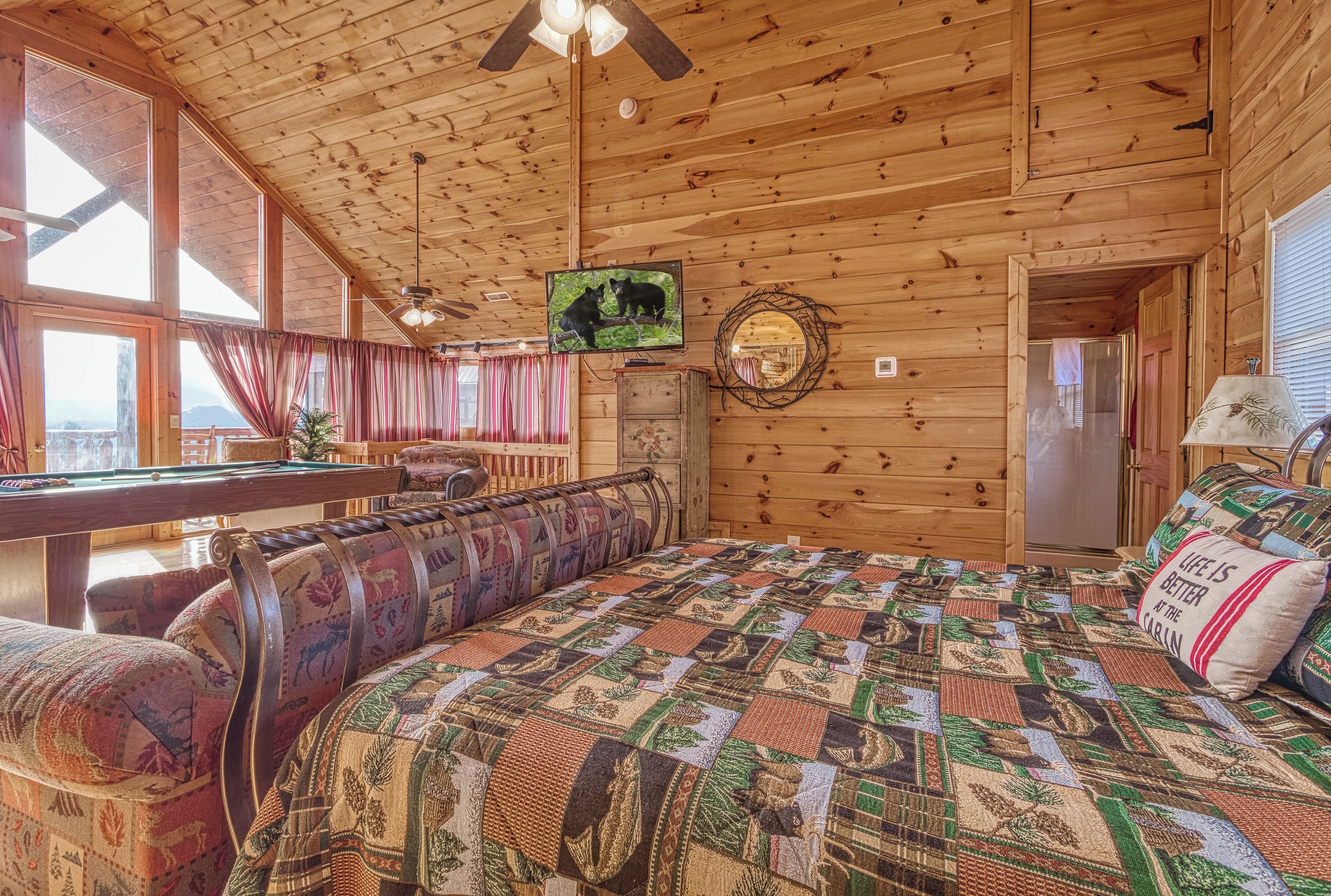 Ein gemütliches Blockhaus-Interieur mit Holzbalkendecke, einem großen Bett mit Quilzdecke, einem Fernseher und einem Billardtisch.