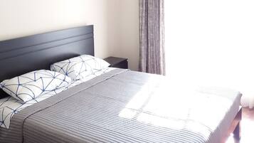 Una cama bien hecha con cubrecama a rayas, cabecera y dos cuadros en la pared.
