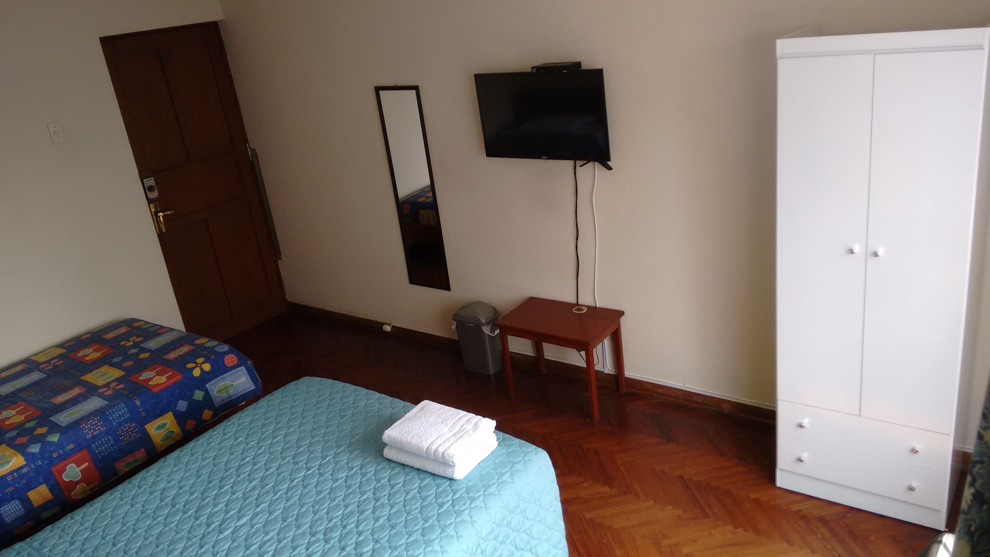 Een slaapkamer met een bed, een garderobe, een televisie en een kleine tafel.