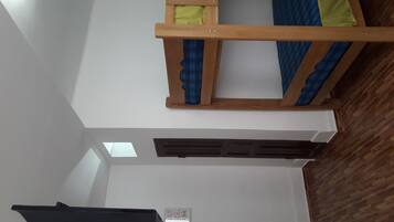 Um quarto com uma cama de solteiro e um mezanino, uma escrivaninha com um computador e uma janela com persianas.