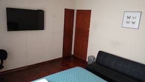 A room with a bed, a sofa, a TV mounted on the wall, and a door. - Guest House Miraflores (Lima)