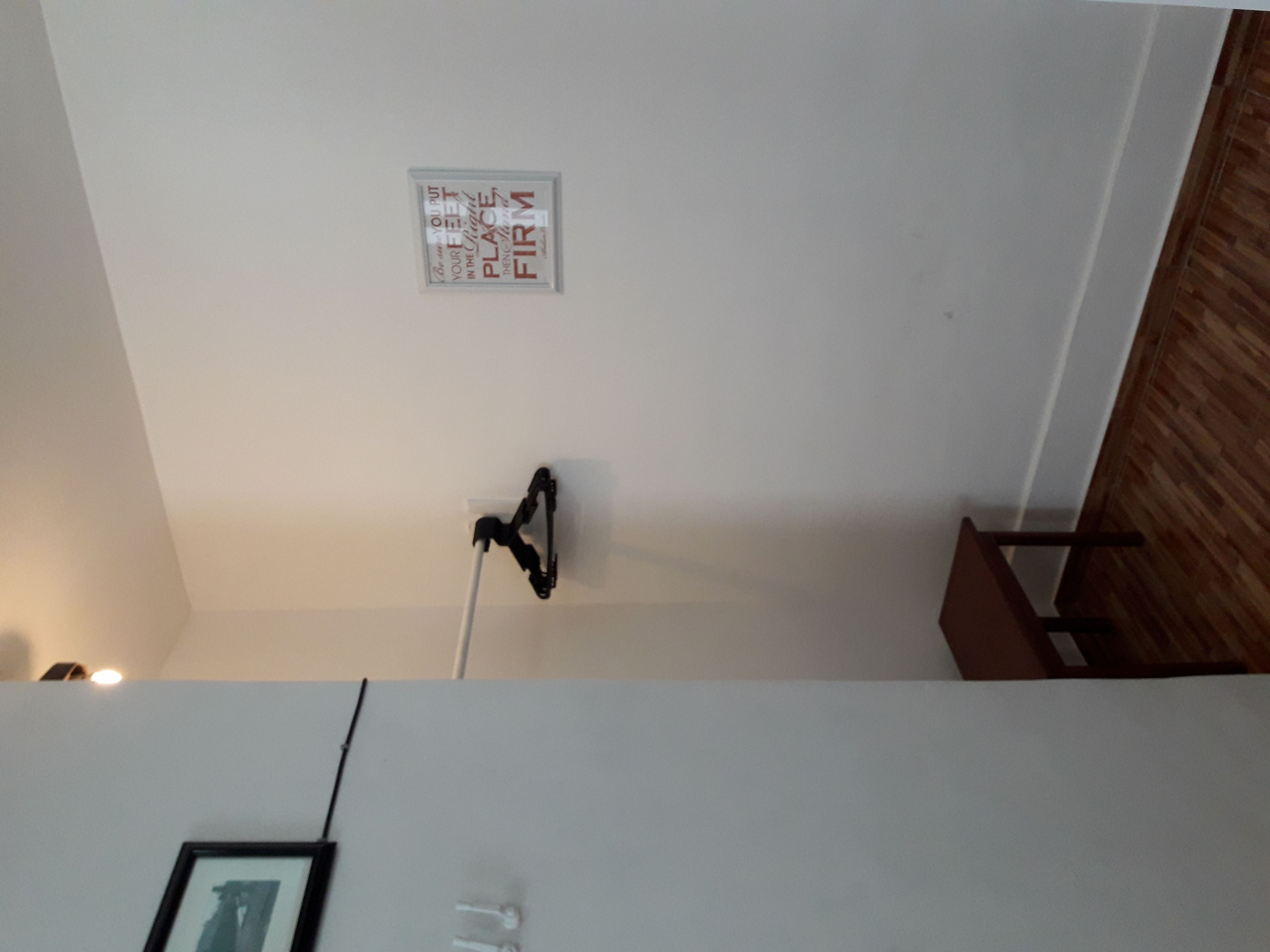 Una habitación con pared blanca, un cuadro enmarcado y una lámpara instalada en el techo.