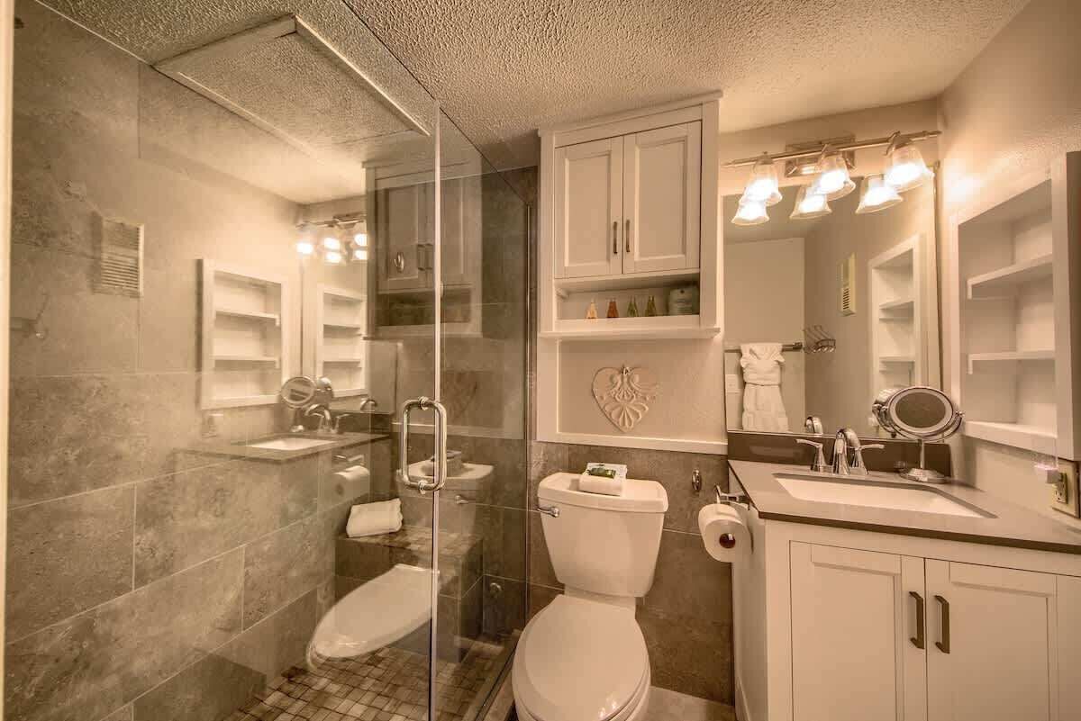 Une salle de bain avec une douche à parois de verre, des toilettes, un lavabo avec un miroir et un meuble-lavabo avec des placards.
