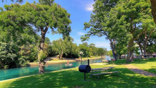 Een park met een picknickplaats, een barbecue en een rivier.