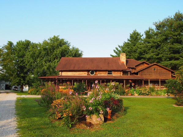 Ein rustikales Holzhaus mit einer großen Veranda, umgeben von einem gepflegten Garten mit verschiedenen Blumen und Pflanzen.