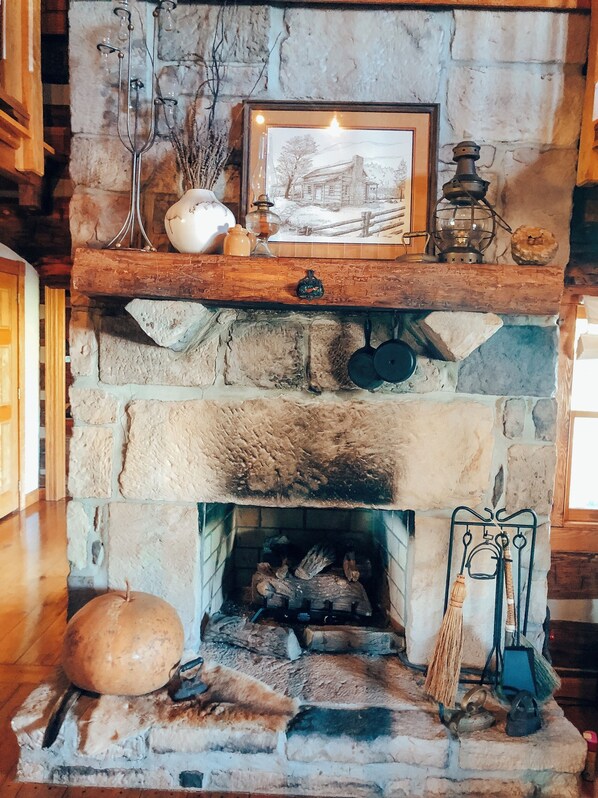 Una chimenea de piedra con un cuadro enmarcado encima, un colgador para ollas y una escoba a la derecha.