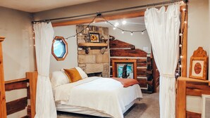 Een knus slaapkamer met een stenen openhaard, een bed met wit beddengoed en een bruine plaid, en een houten hoofdbord.