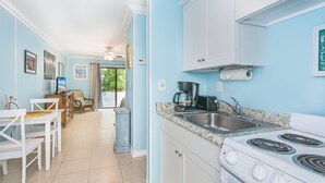 A kitchen with white cabinets, a stove, and a sink. There is a dining area with a table and chairs. - Steps to Beach, Private Boutique Bungalow (Juno Beach)