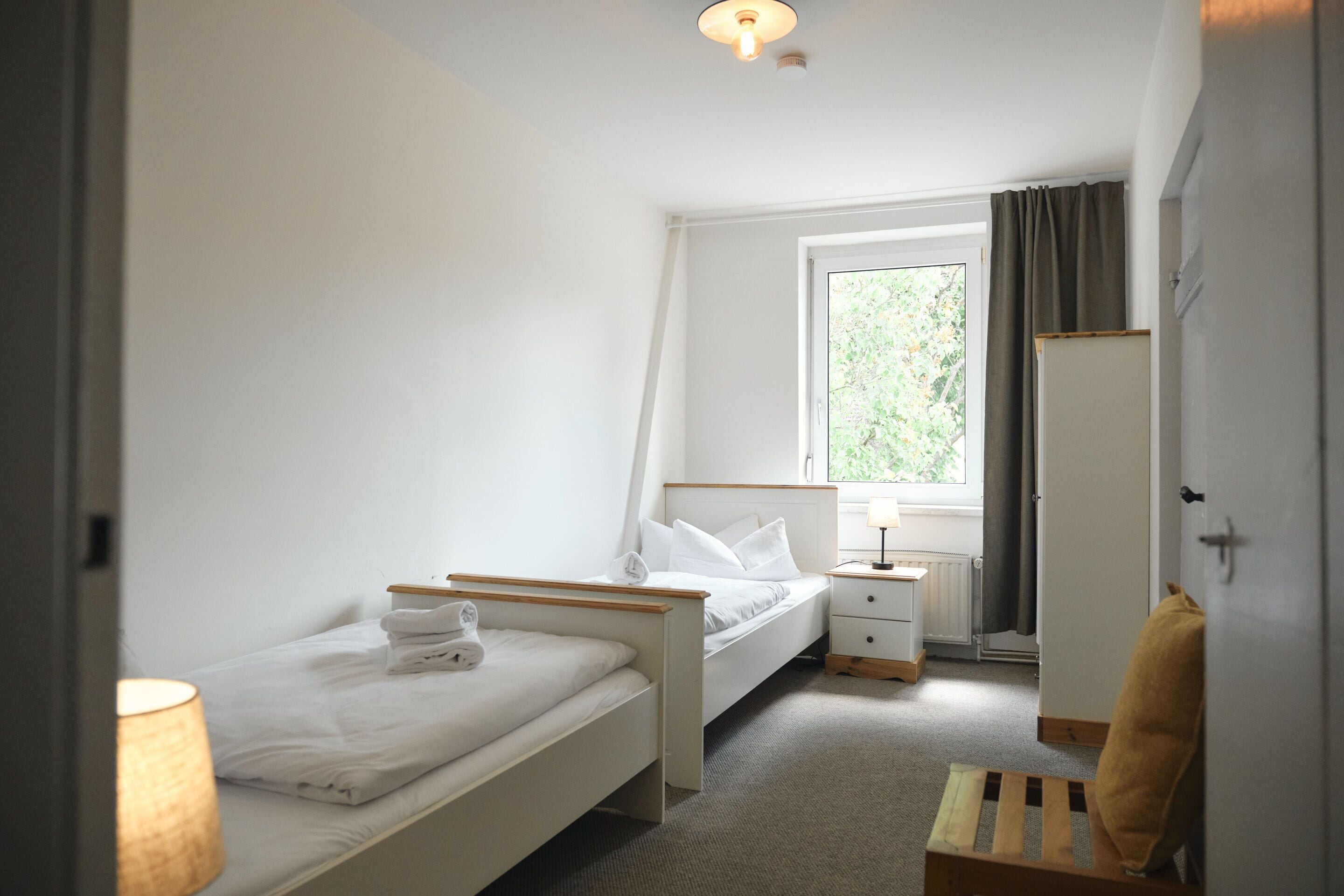 Ein kleines, ordentlich eingerichtetes Schlafzimmer mit einem Einzelbett, einem Nachttisch und einem Sessel.