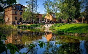 A riverside view with a building featuring a mix of traditional and modern architecture, a grassy area, and a calm water body reflecting the surroundings. - Muehle Tornow (Fürstenberg-Havel)