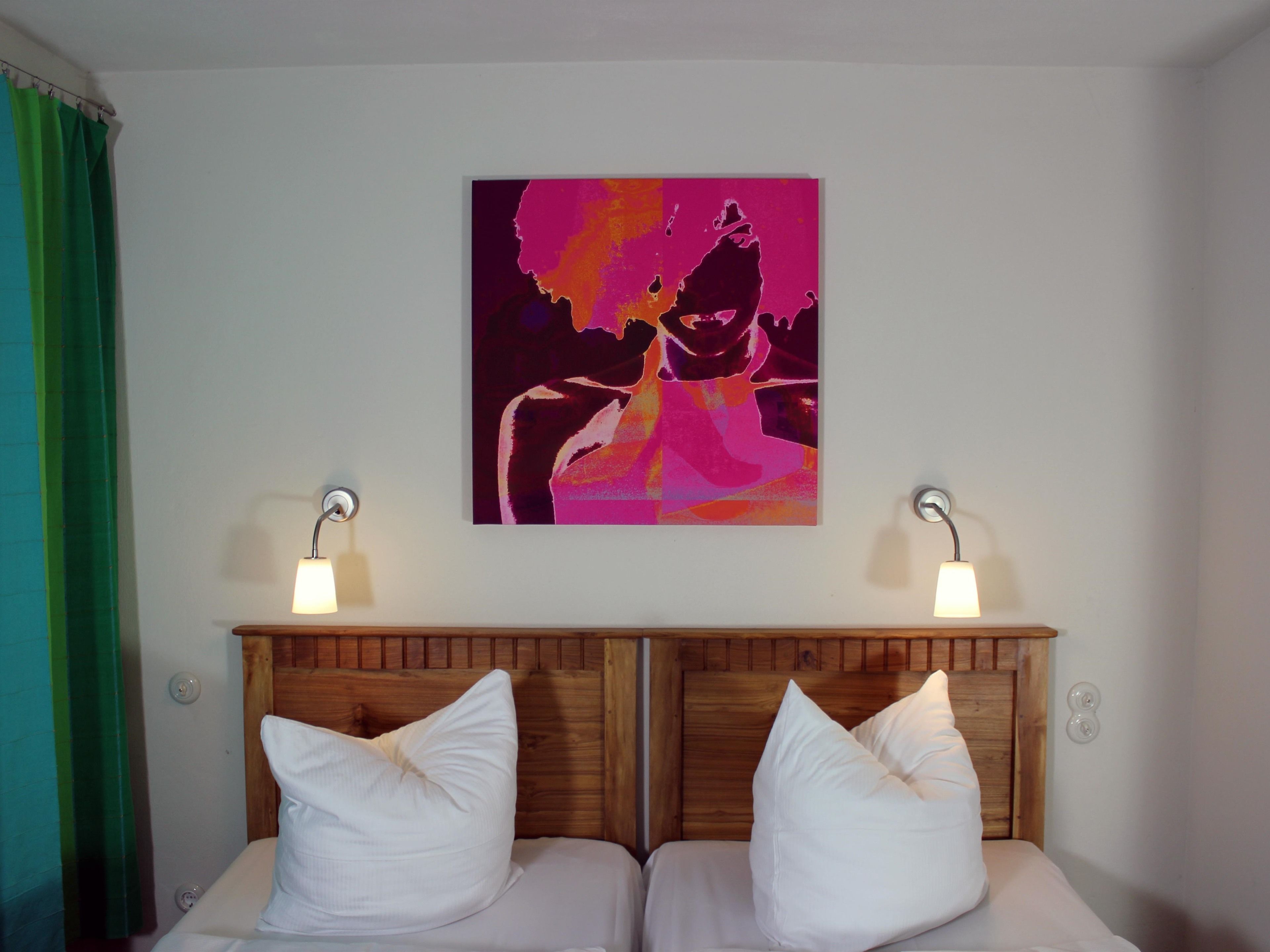 A bedroom with a wooden headboard, two white pillows, and a colorful abstract painting on the wall.