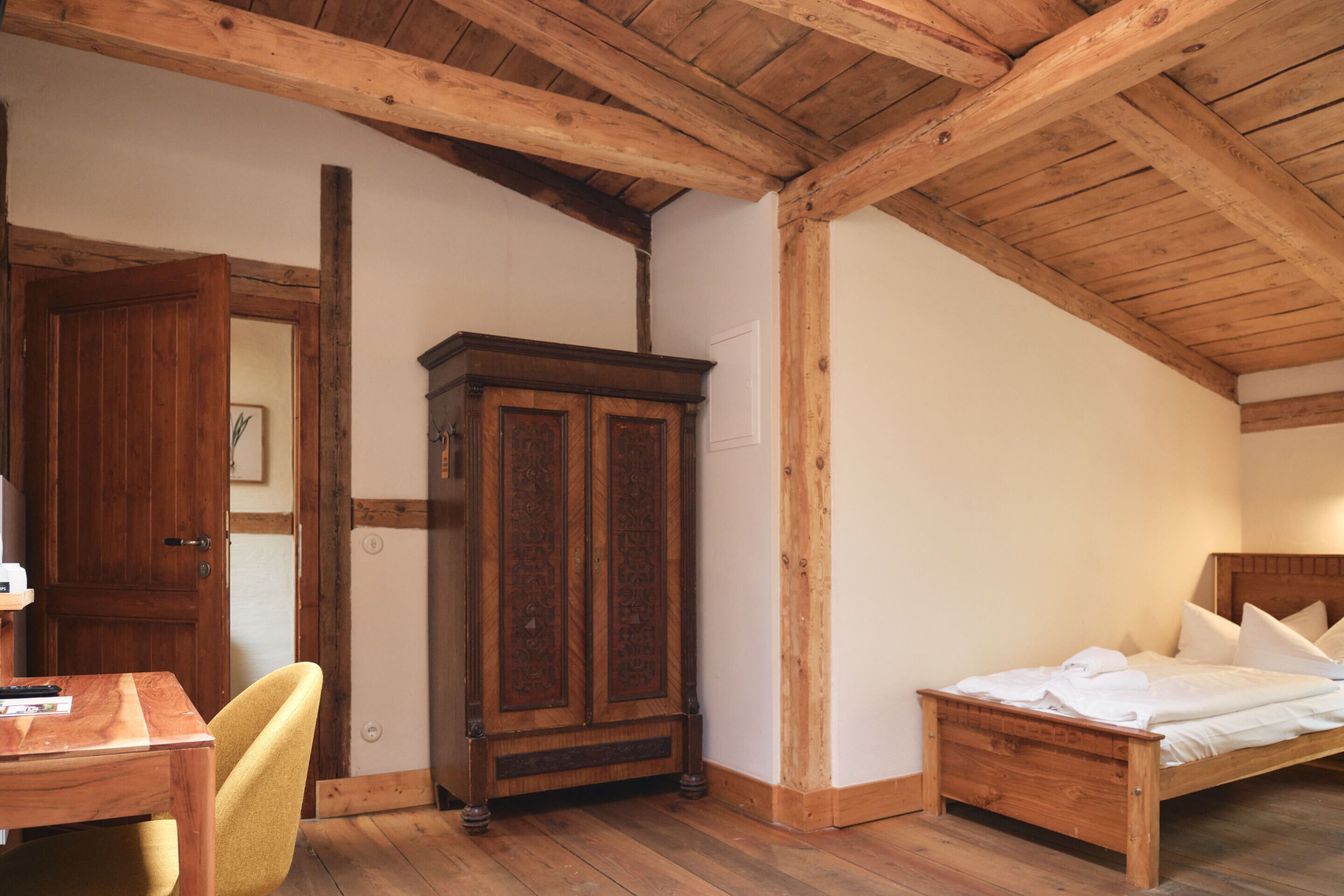 Un dormitorio con techo, cama, armario y escritorio de madera, y una silla.