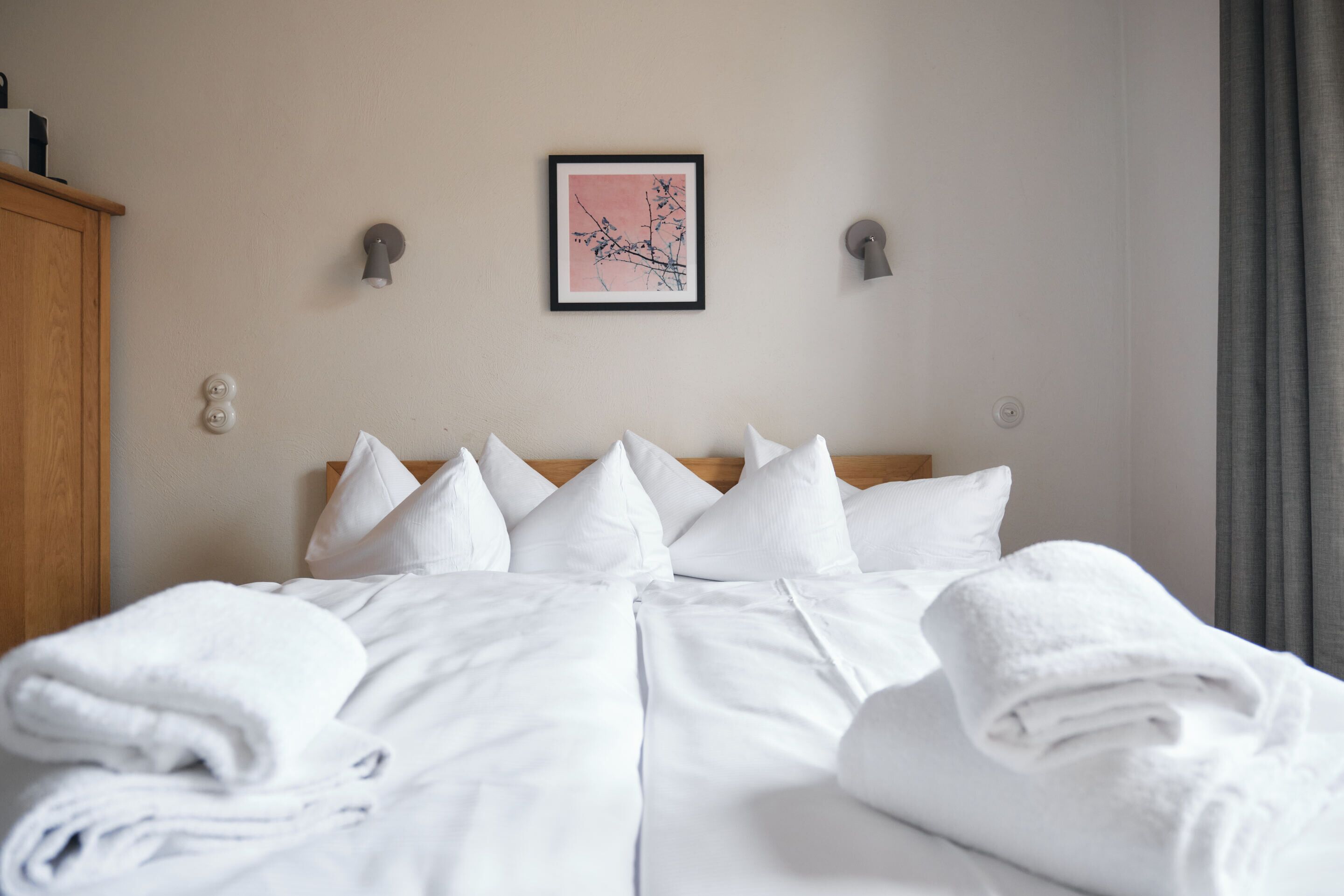 Un letto rifatto con lenzuola e cuscini bianchi, un quadro appeso alla parete e un armadio in legno.