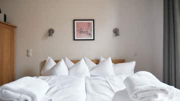 Un letto rifatto con lenzuola e cuscini bianchi, un quadro appeso alla parete e un armadio in legno.