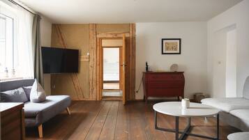 A living room with a wooden floor, a grey sofa, a red dresser, a white coffee table, and a TV mounted on the wall.