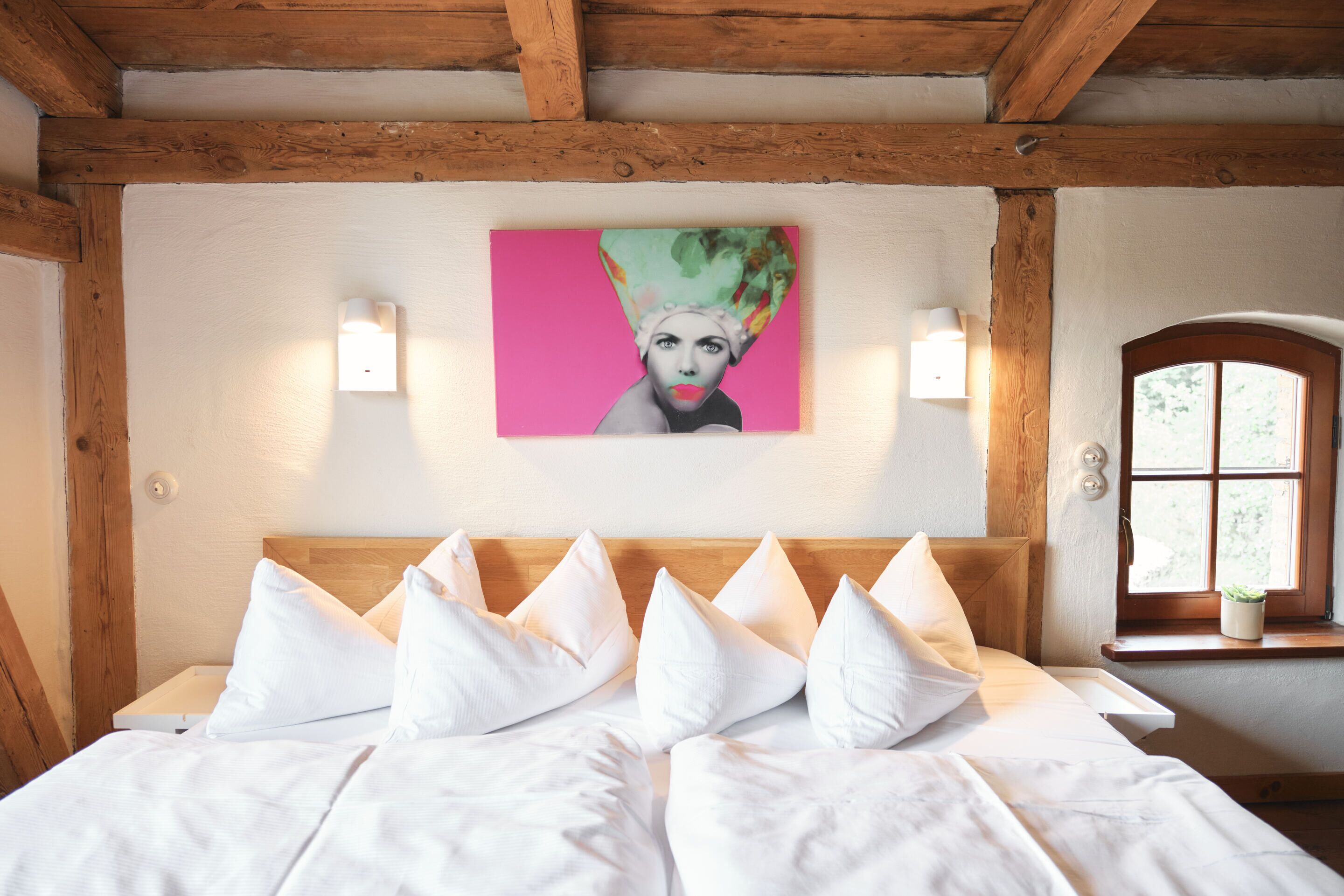 A bedroom with a wooden headboard, white bedding, and a painting above the bed.