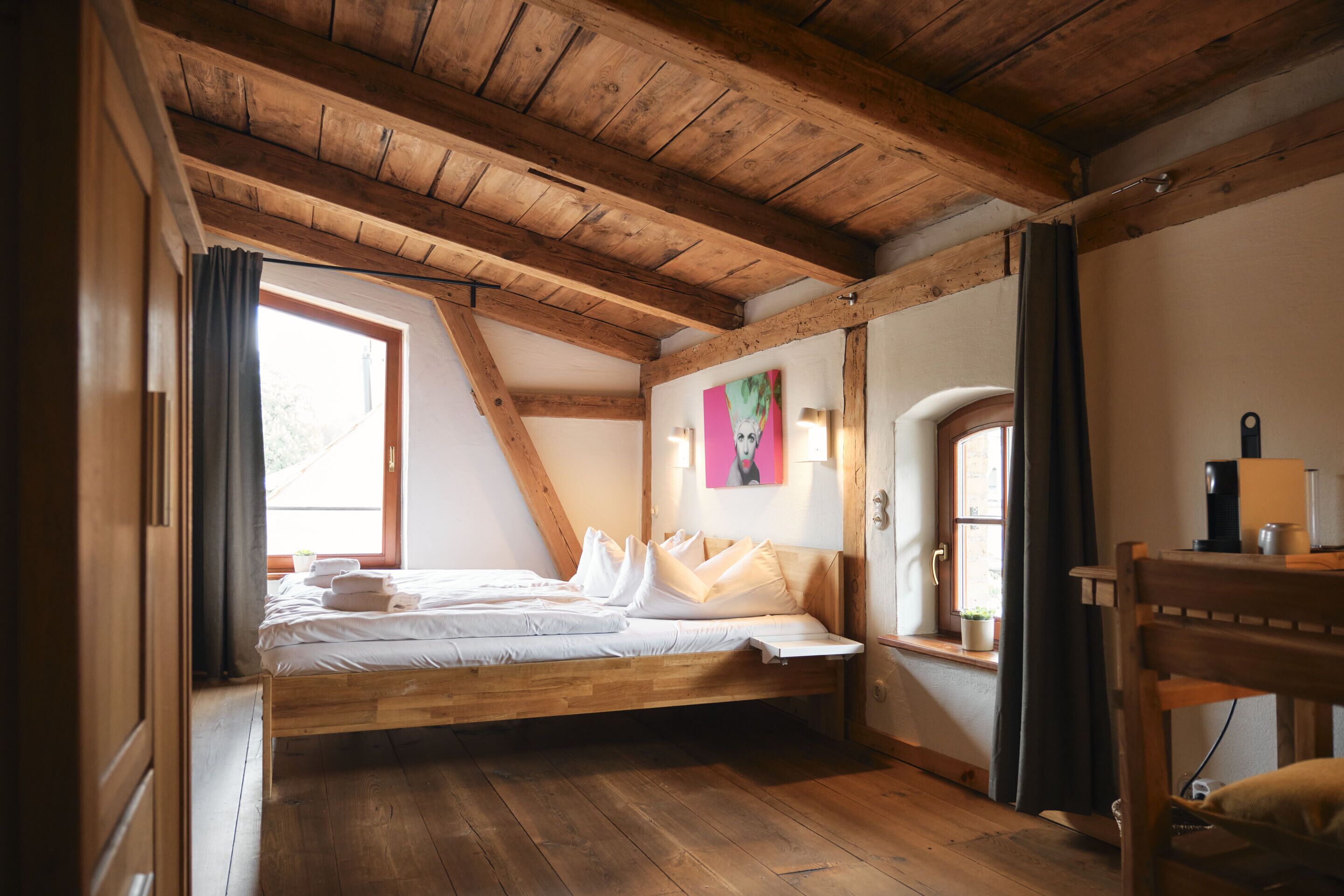 Una camera da letto con soffitto in legno, un letto, una finestra, una scrivania e una sedia.