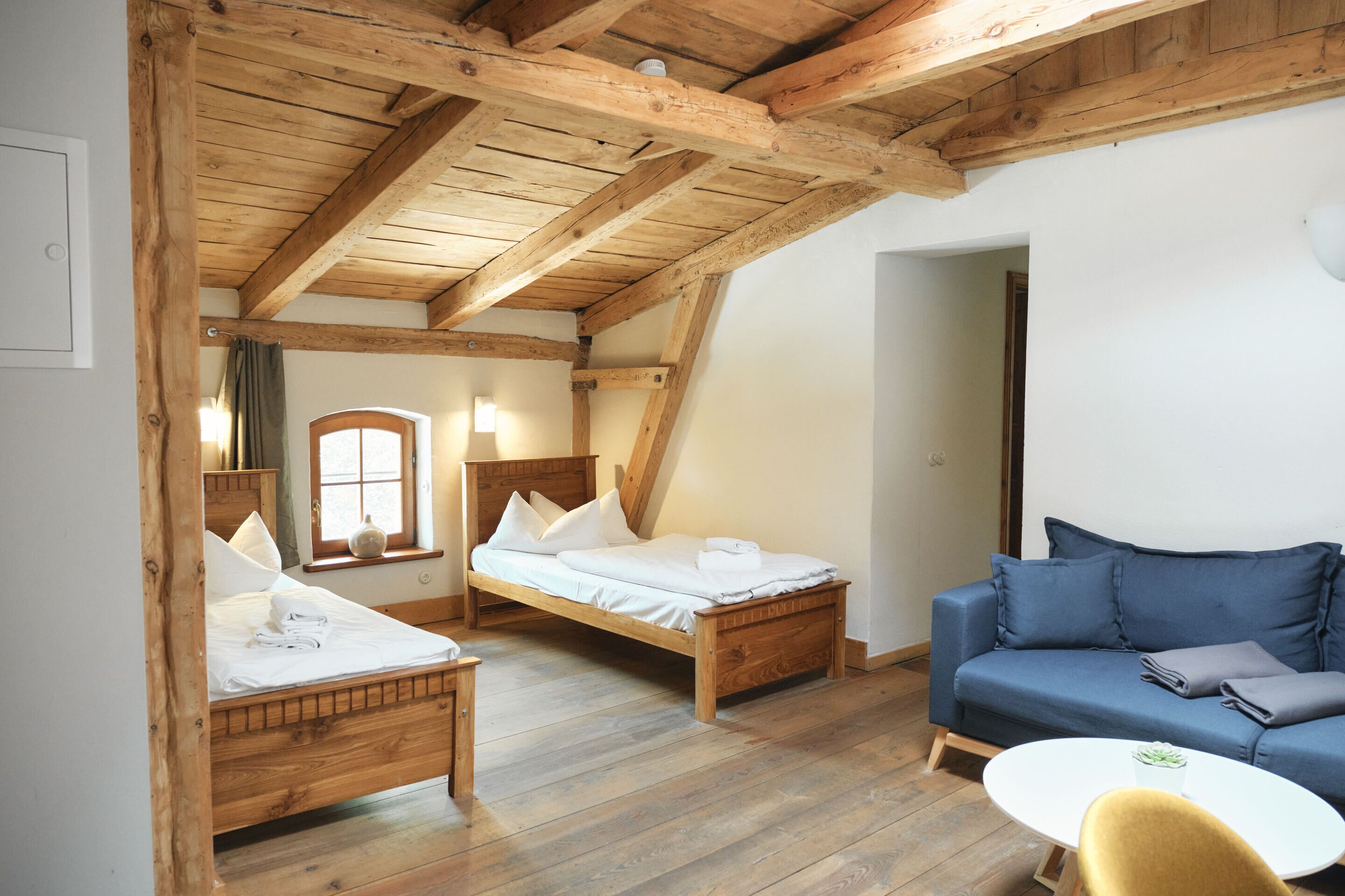 Una habitación con vigas de madera, una cama, un sofá y una pequeña mesa.