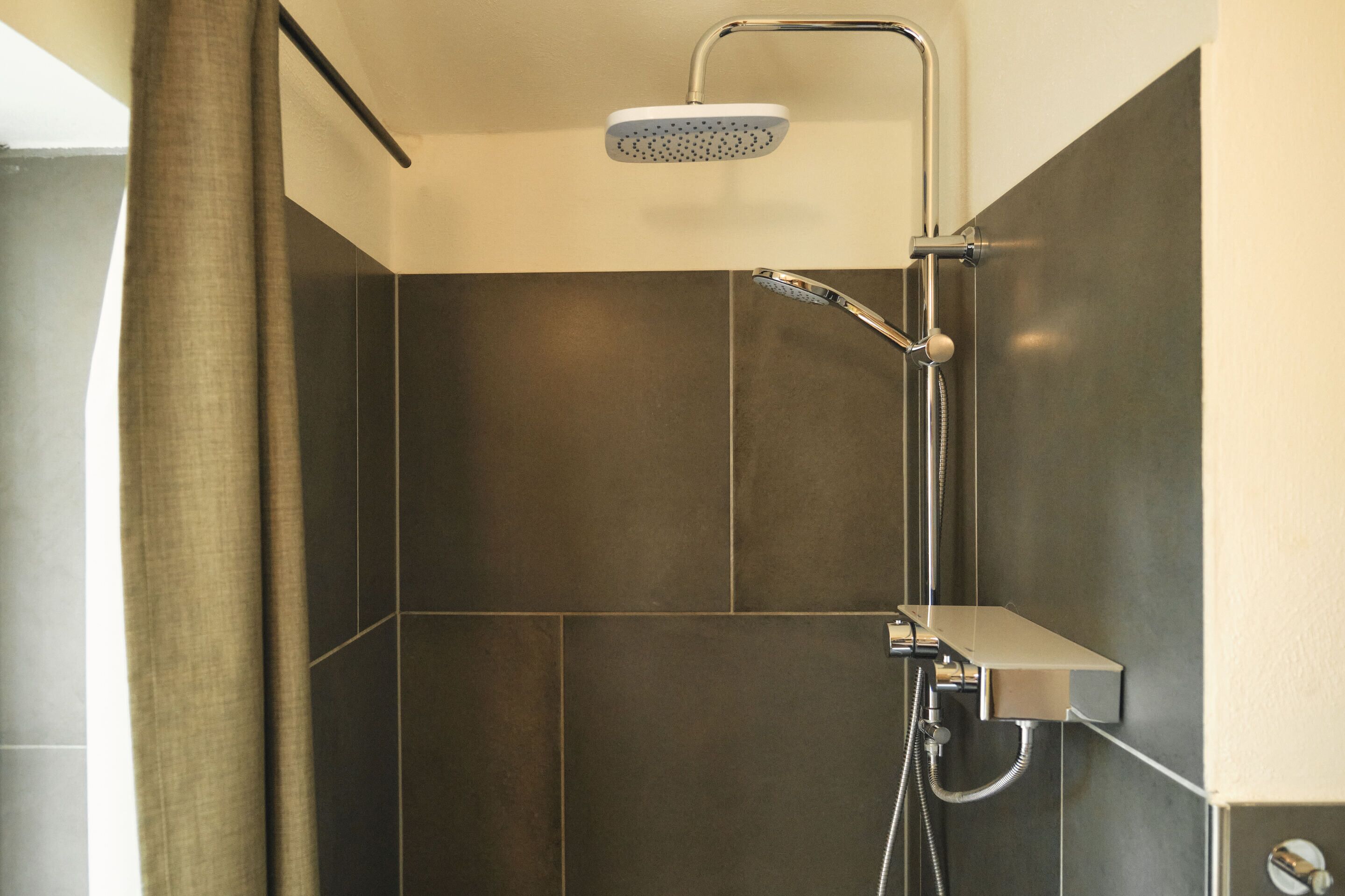 Una ducha moderna con cabezal de ducha manual y panel de control en la pared.