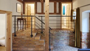 Una escalera con vigas de madera y paredes de ladrillo, que conduce a una habitación con cama y sillón.