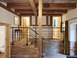 Una escalera con vigas de madera y paredes de ladrillo, que conduce a una habitación con cama y sillón.