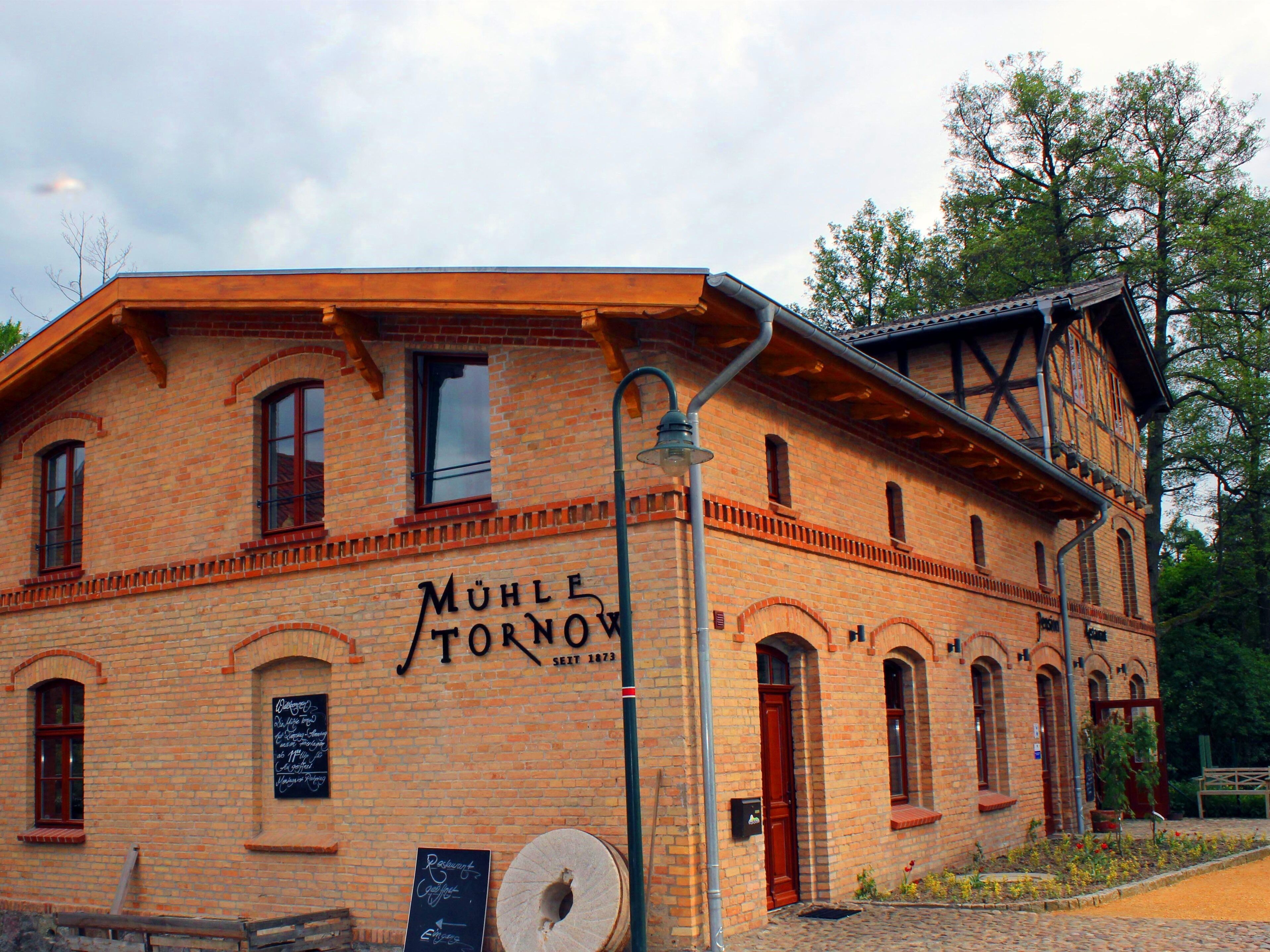 A brick building with arched windows and a sign reading "Mühle Stornow" dating back to 1873.