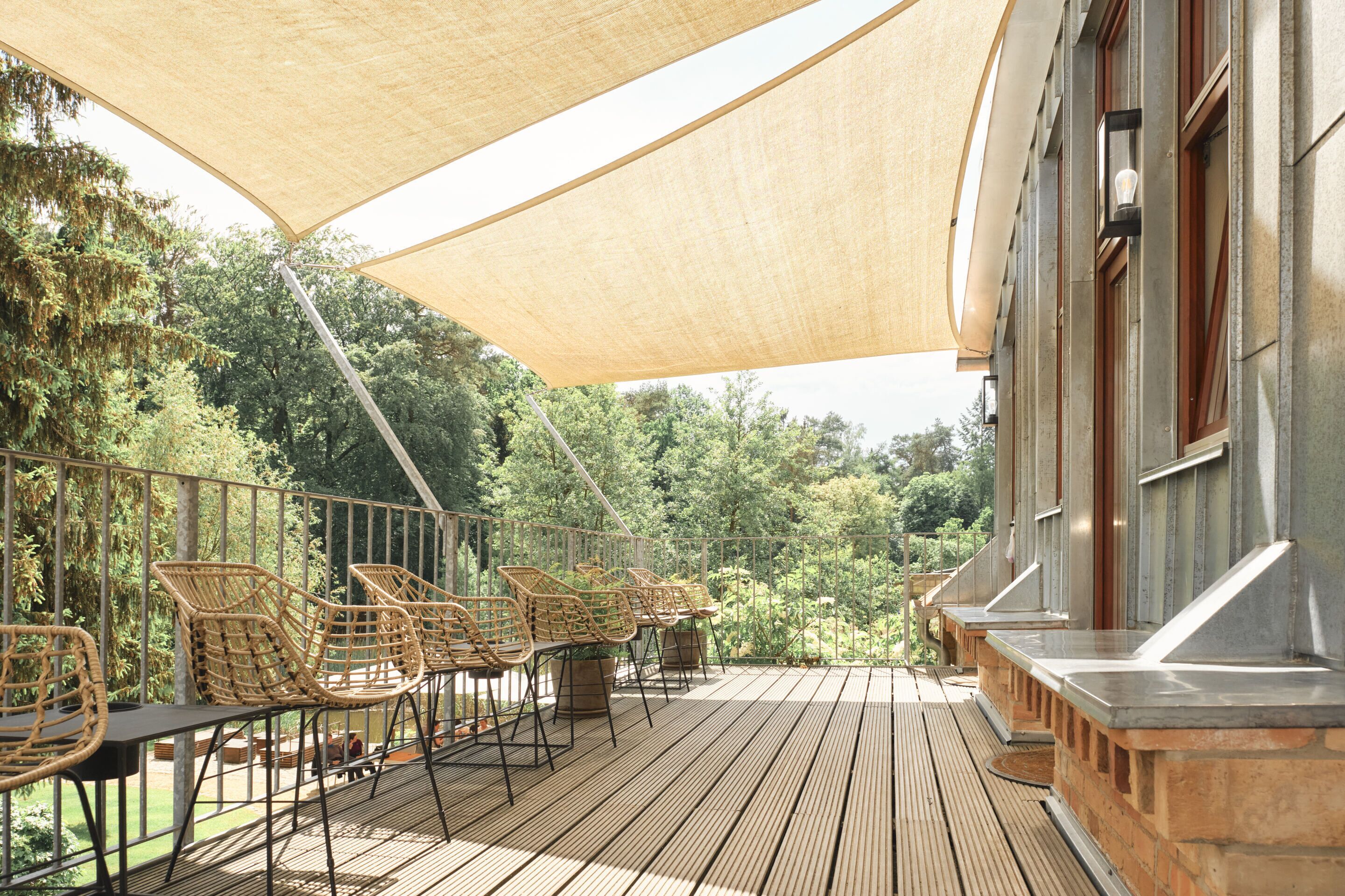 Une terrasse extérieure avec des fauteuils en osier et une table, donnant sur un jardin luxuriant.