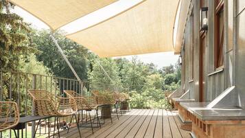Une terrasse extérieure avec des fauteuils en osier et une table, donnant sur un jardin luxuriant.