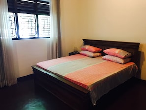 A single bed with a wooden headboard, a pink and white bedspread, and multiple pillows.