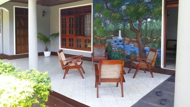 A covered outdoor seating area with wooden chairs and a mural of a waterfall and trees. - Onix Villa (Galle)
