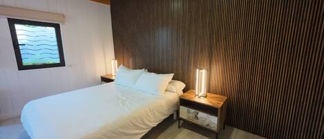 Un dormitorio con cama, dos mesitas de noche, una lámpara de noche, una ventana con vistas y una pared de listones de madera.