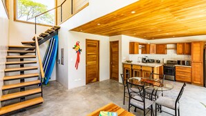 Eine moderne Küche mit Holzausbau, ein Essbereich mit Glastisch und Stühlen sowie eine Treppe mit blauer Geländer.