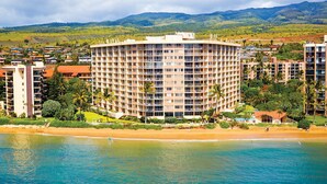 A multi-story hotel with a central courtyard, surrounded by lush greenery and a beach.
