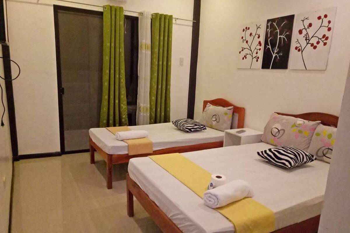 A hotel room with two single beds, a wooden headboard, a small bedside table, and a wall with three framed artworks.