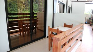 Una habitación con puerta de vidrio corrediza que da a un balcón, un banco de madera y una mesa con sillas.
