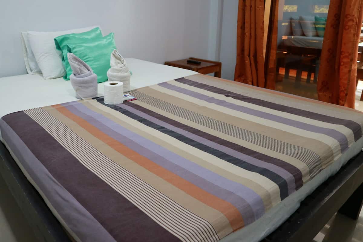 A hotel room with a bed, pillows, a striped blanket, a towel, and a roll of toilet paper.