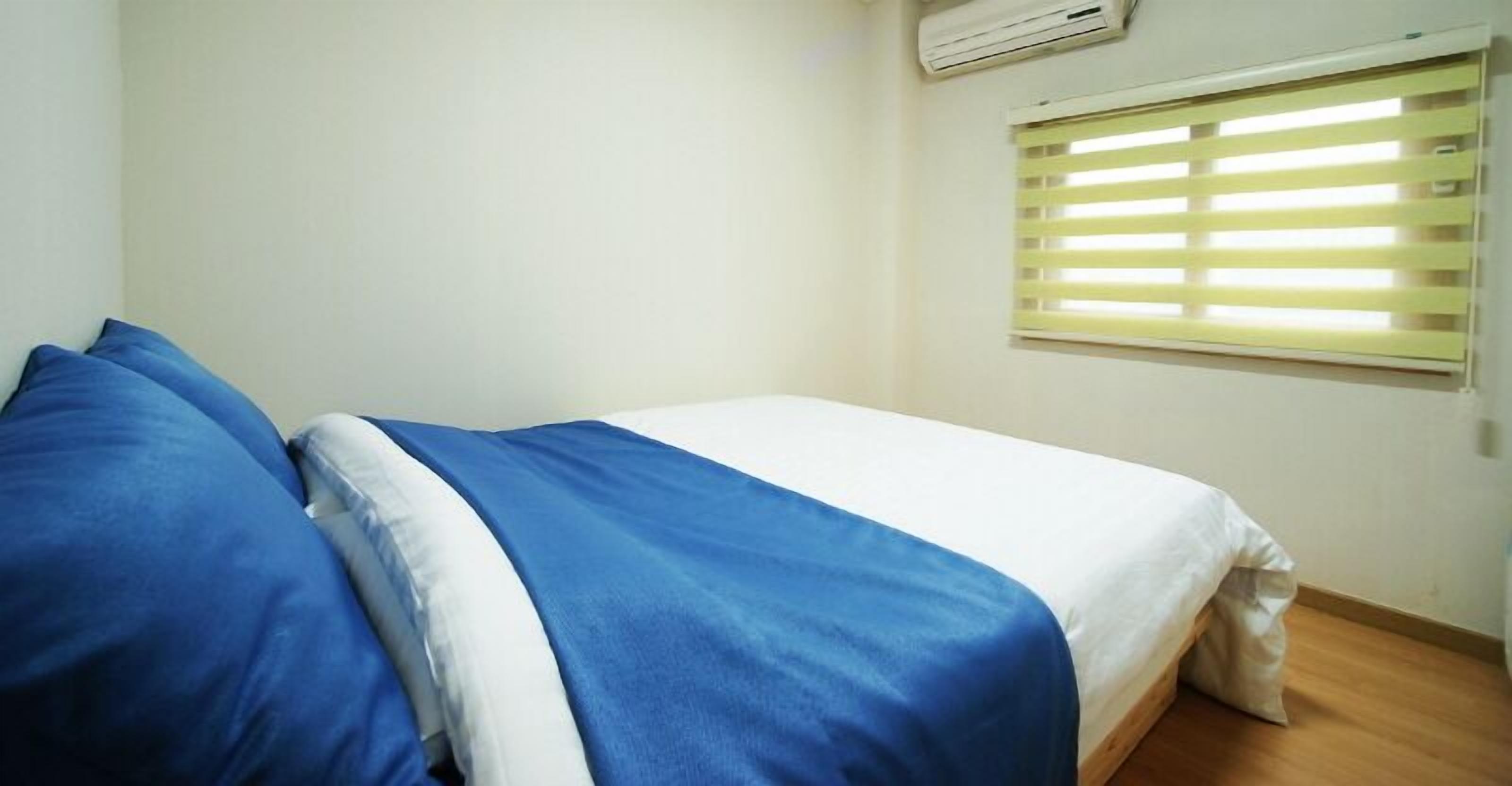 Une chambre à coucher avec un lit, une fenêtre avec des stores et un appareil de climatisation.