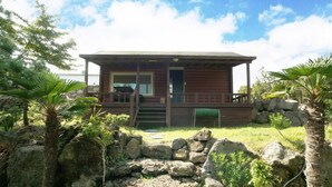 Une cabane en bois dotée d’une véranda, entourée de rochers et de plantes tropicales.