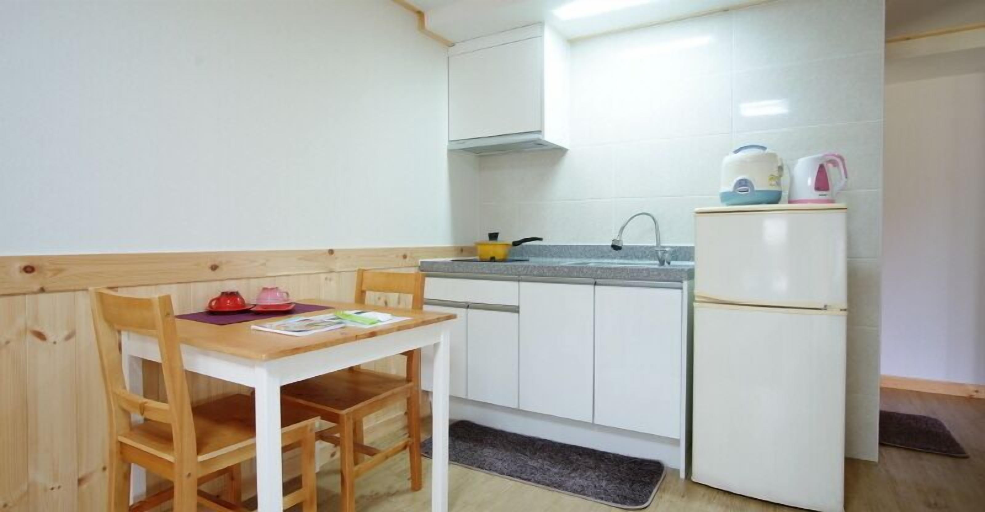 A small kitchenette with a wooden table, chairs, a white refrigerator, a sink, and a stove.