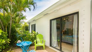 A patio with a table and chairs, surrounded by lush greenery and a large sliding glass door leading to a pool. - Prime Location. Hidden Gem. Steps to Beach. Boutique Bungalow. Pet Friendly.  (Juno Beach)