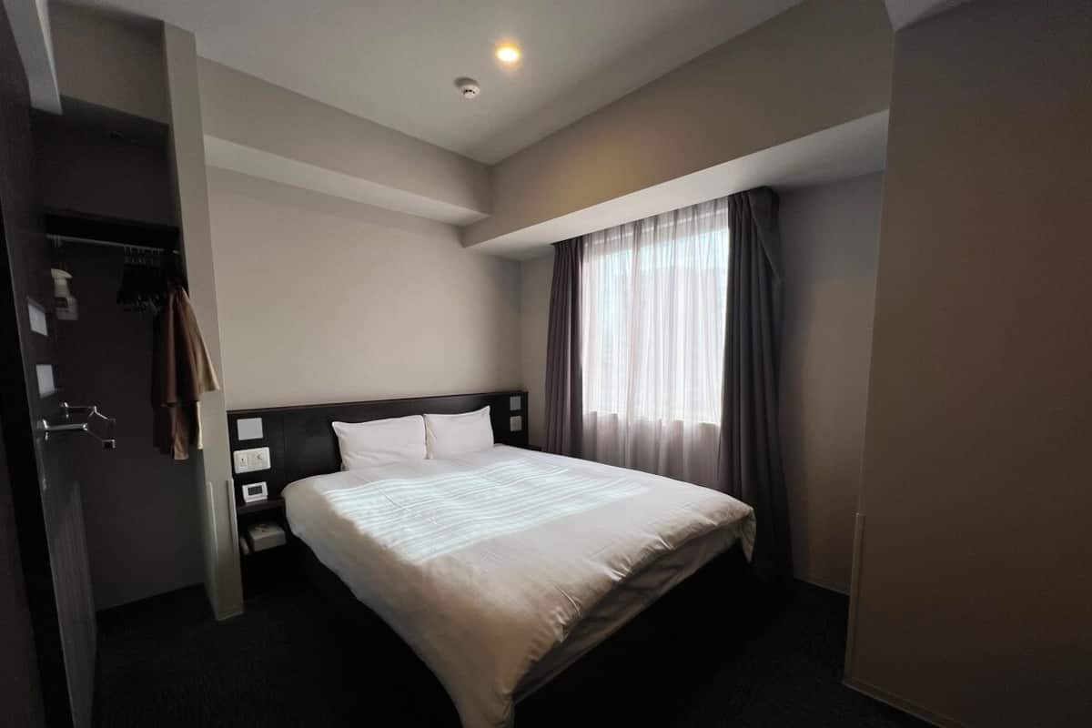 A hotel room with a bed, a nightstand, a wardrobe, and a window with curtains.