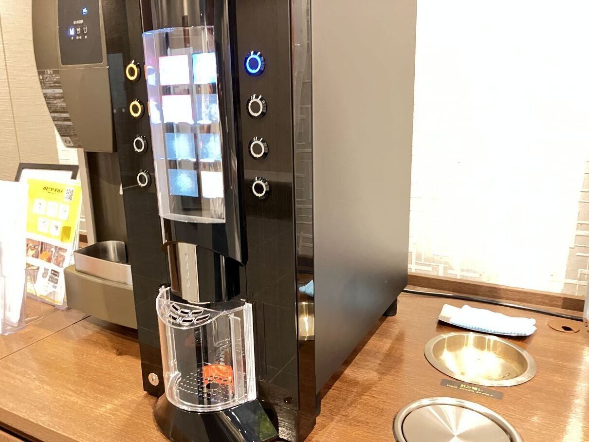 A coffee machine with a digital display and buttons, a trash bin, and a stainless steel sink.